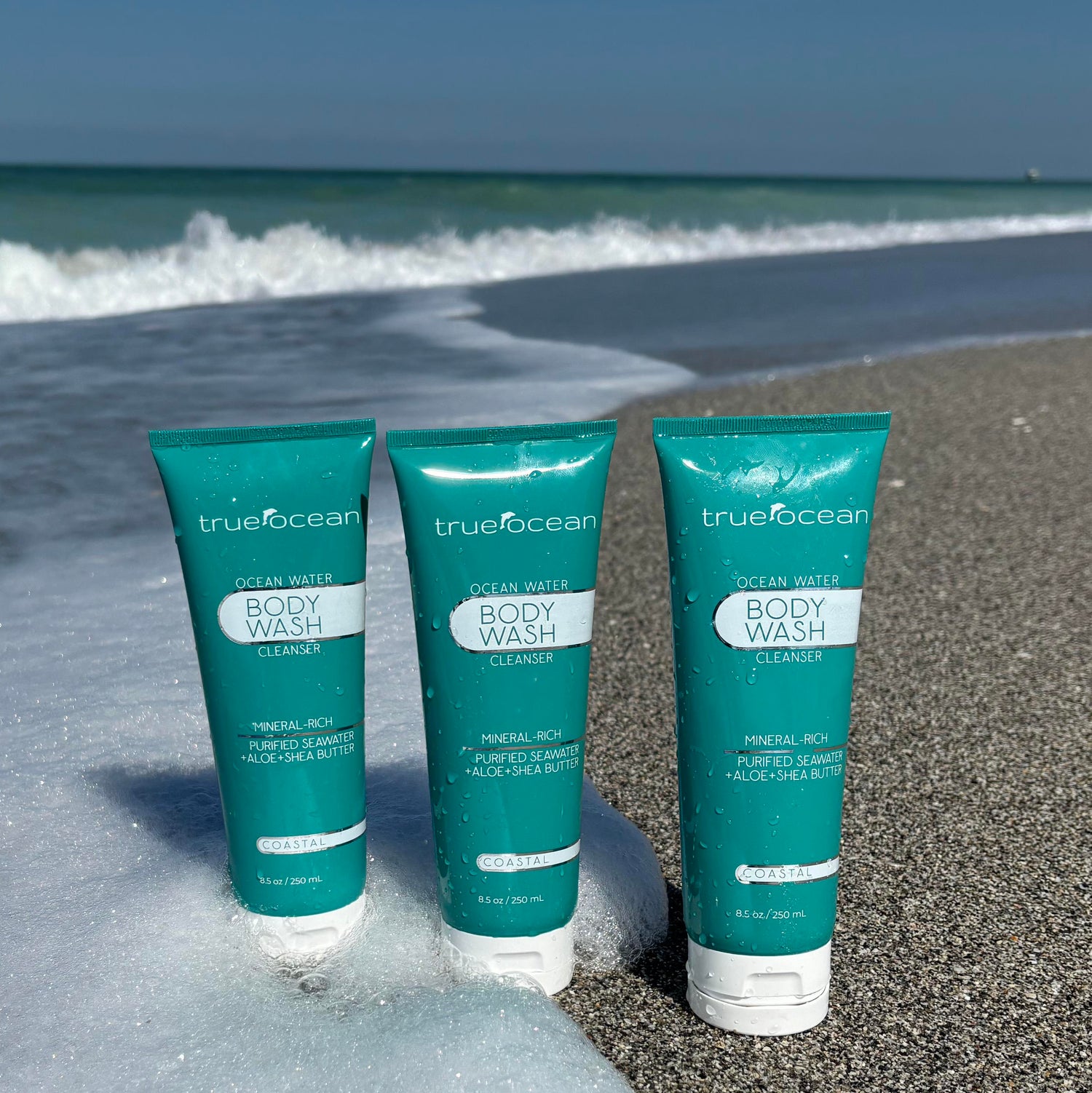 True Ocean Body Wash cleanser bottles on the beach with crashing waves in the background